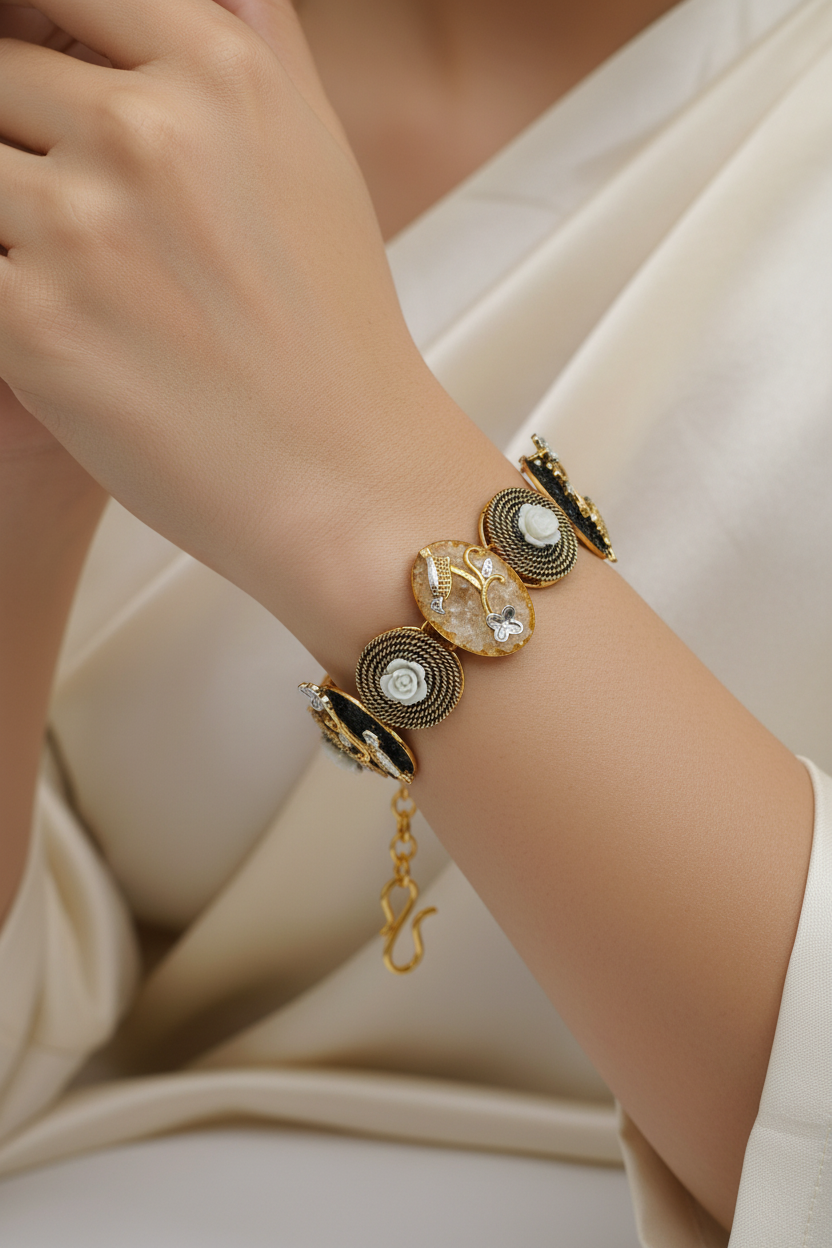 A gold-toned bracelet featuring alternating oval and round charms with white and black inlays, set against a plain light gray background.