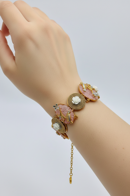 A gold-plated bracelet featuring oval pink stone inlays, small gold floral motifs, and clear rhinestone accents, laid out diagonally on a plain white surface.
